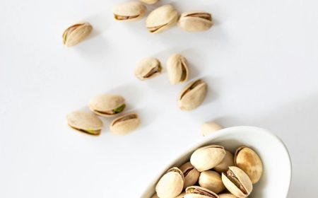 Pistachio nuts in a white bowl on a white background, top view.