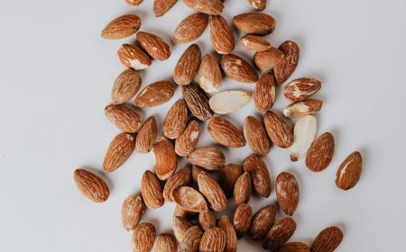 Top view of scattered raw almonds around a pink ceramic bowl on a clean white surface.